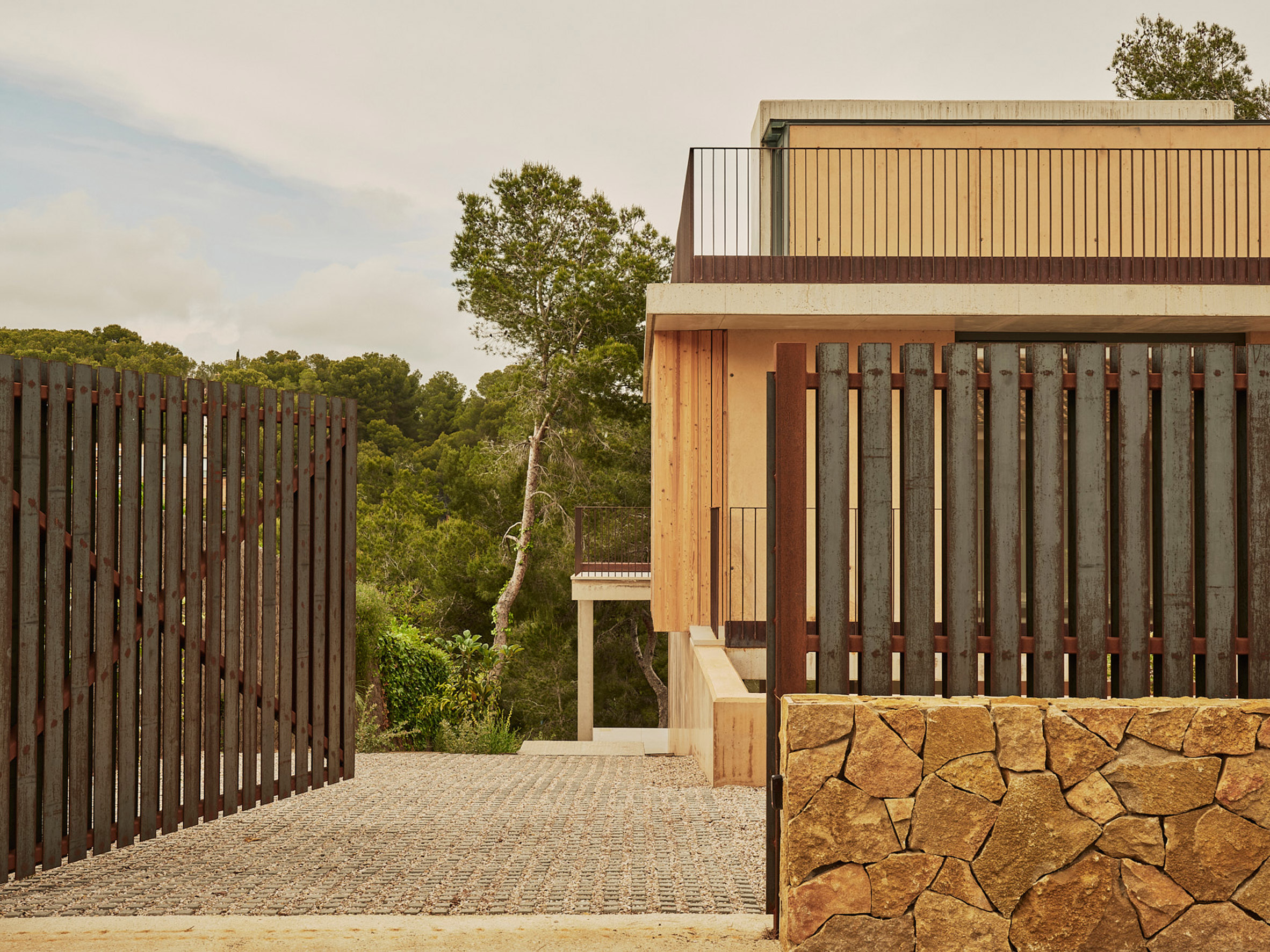 La Casa en Cala Tamarit se organiza en dos volúmenes escalonados que generan balcones y terrazas exteriores directamente vinculadas al desnivel natural del terreno. 