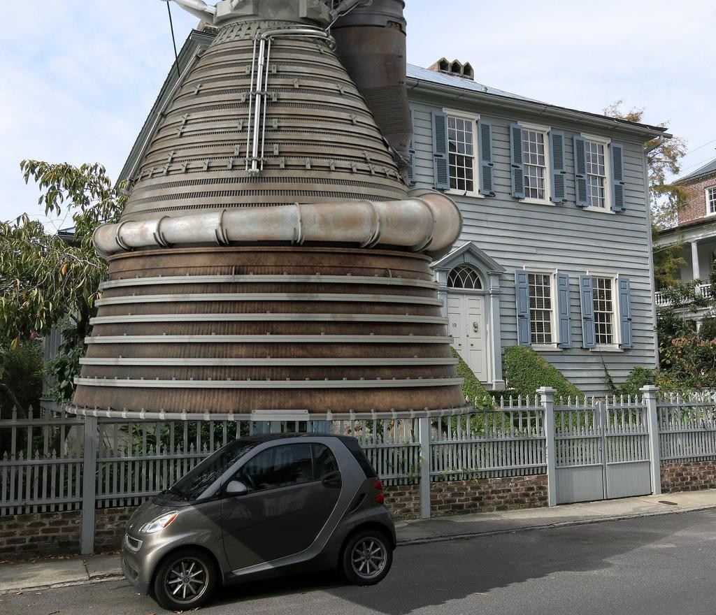 Motor de cohete M-1 (4,2 m de diámetro) sobre un Smart (2,6 m de largo) y junto a una casa típica estadounidense cohete