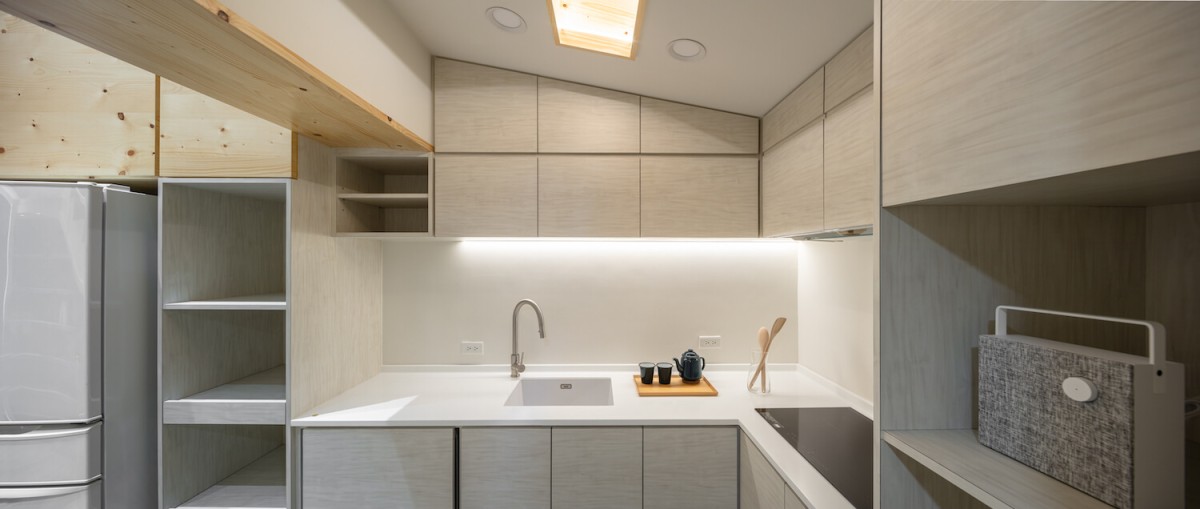 La cocina abierta se diferencia del resto de los espacios por el empleo de la madera contrachapada de los armarios en color gris.