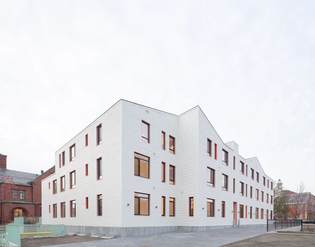 Las paredes exteriores están revestidas de fibrocemento en tonos vainilla y rosa pálido, donde se abren ventanas de diversos tamaños.