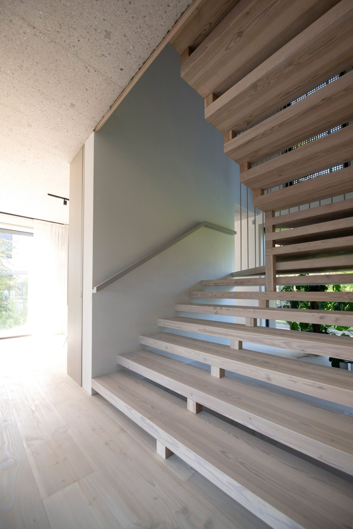 La escalera está realizada con madera del mismo tono que el suelo y presenta una estética moderna por su esbeltez.