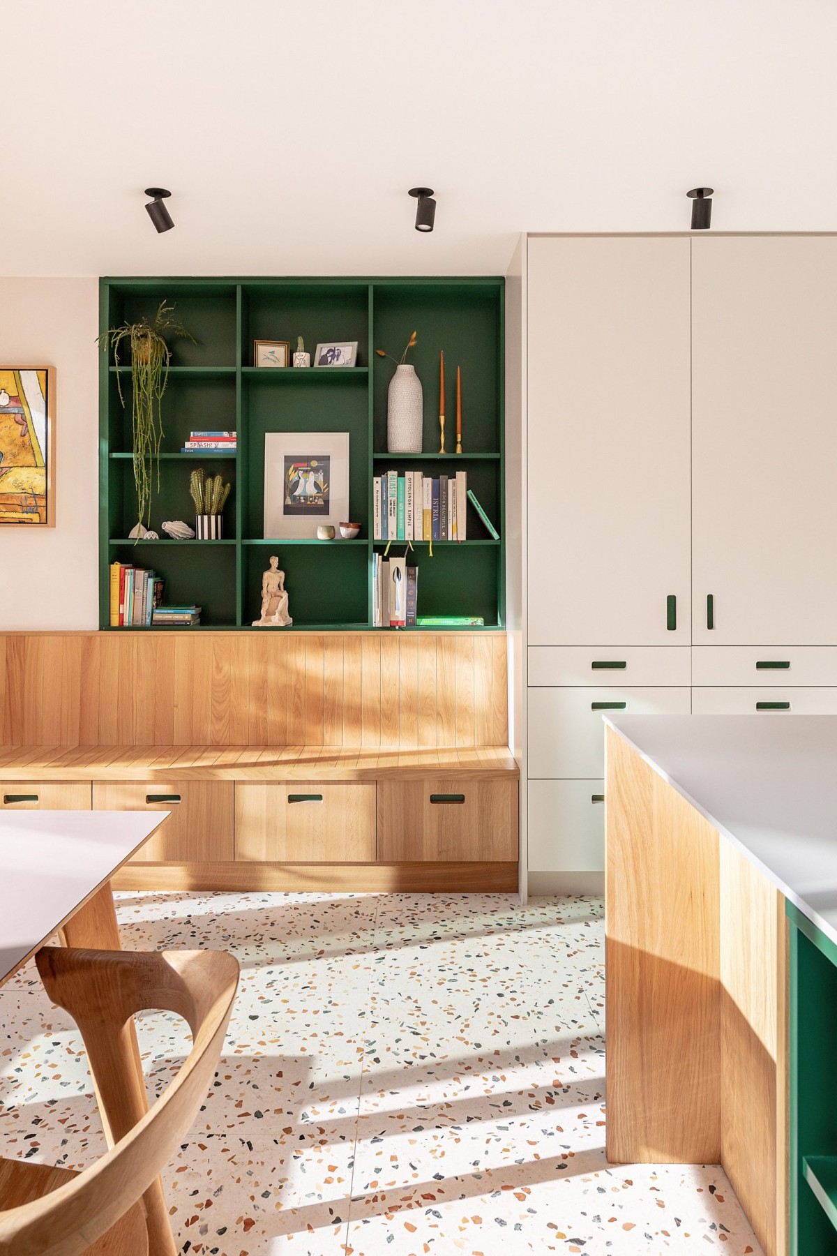 El diseño interior de la casa incorpora muebles modernos y detalles en roble europeo, incluyendo un banco de madera empotrado y estanterías verdes.