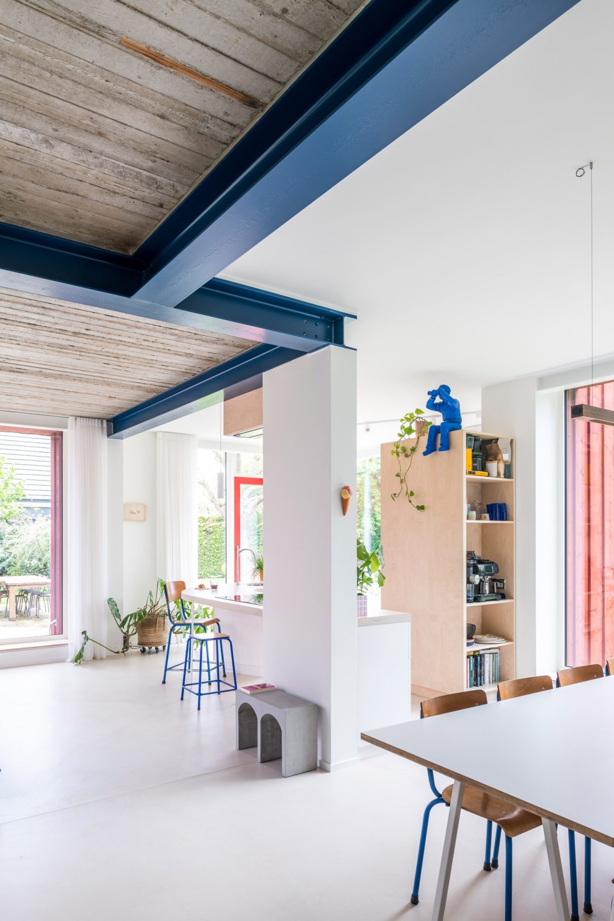 Las paredes blancas y accesorios de madera pálida contrasta con las vigas de acero azul y los techos de hormigón visto.