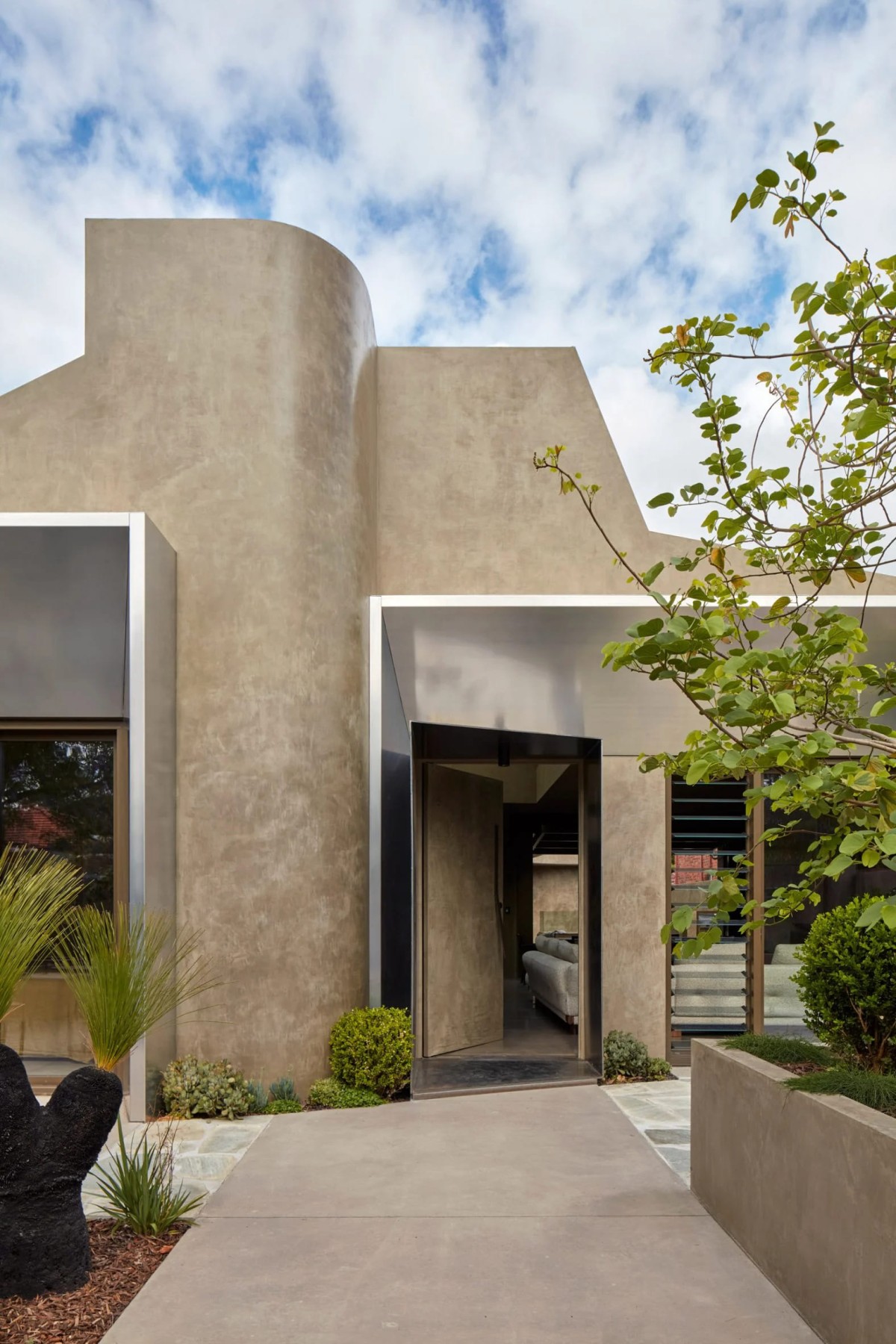La vivienda destaca por su uso de un revoco de cáñamo en tono oliva combinado con detalles de aluminio y hormigón escultural.