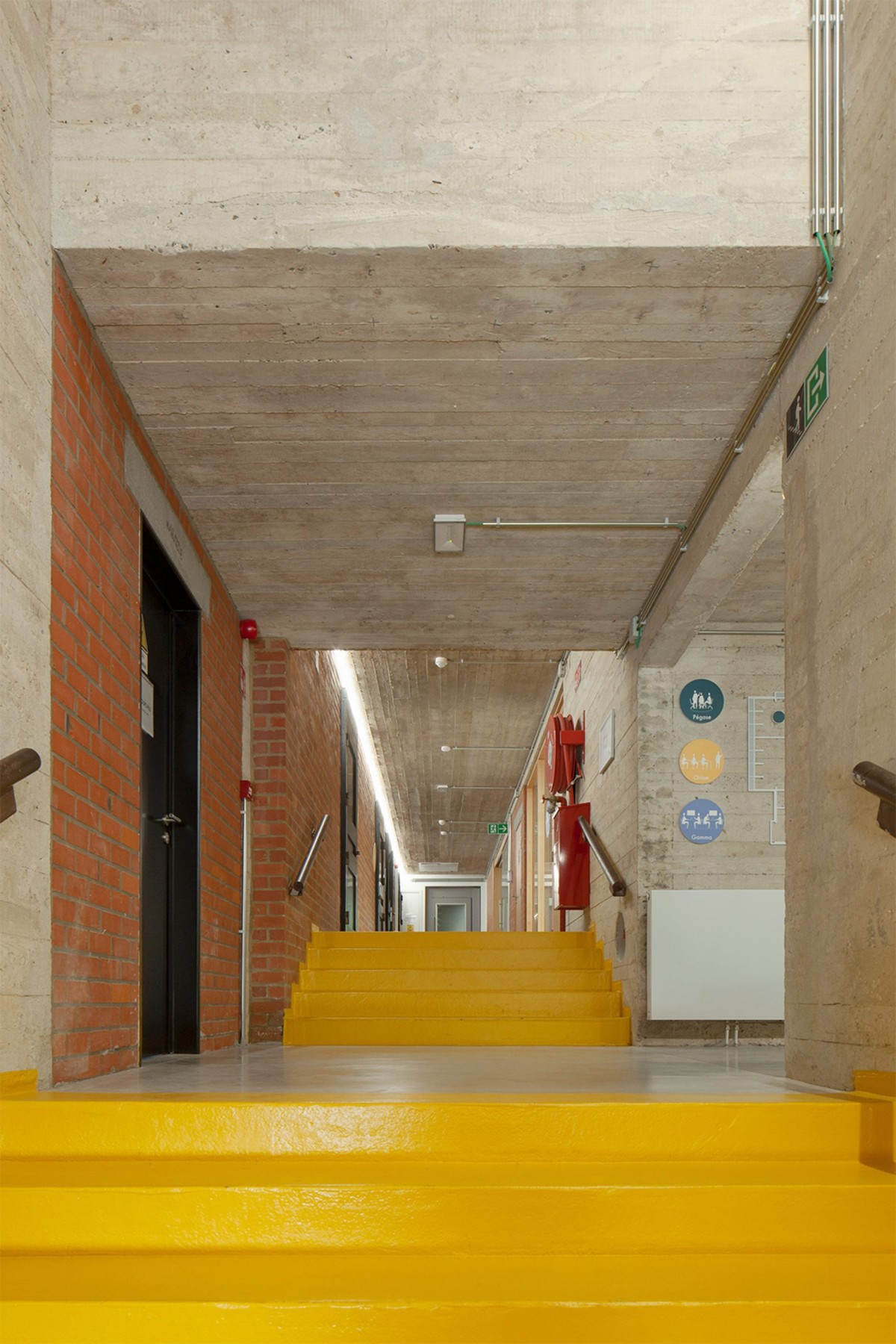 El amarillo de la escalera principal resalta junto al rojo del ladrillo, creando una paleta de colores gráficos que da vida al edificio.