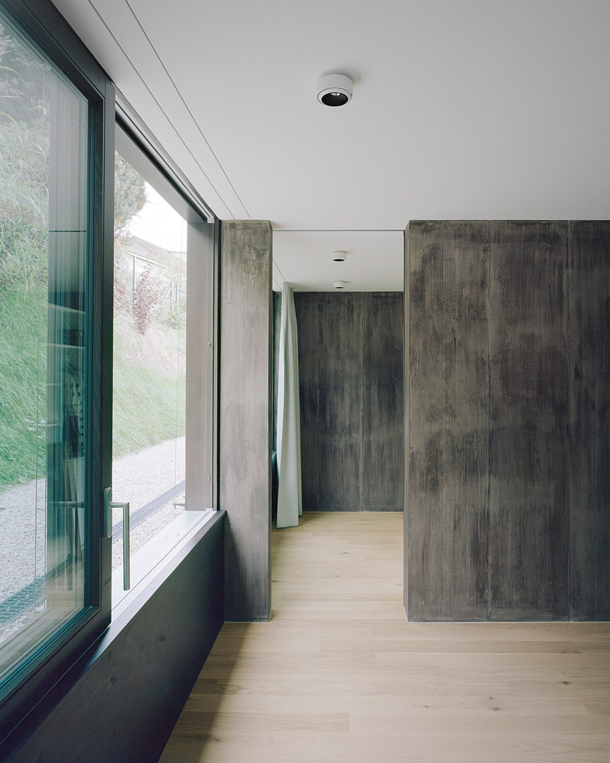 Las superficies blancas, los suelos de madera clara y las cortinas grises crean una atmósfera suave y luminosa que dialoga con la contundencia del hormigón.