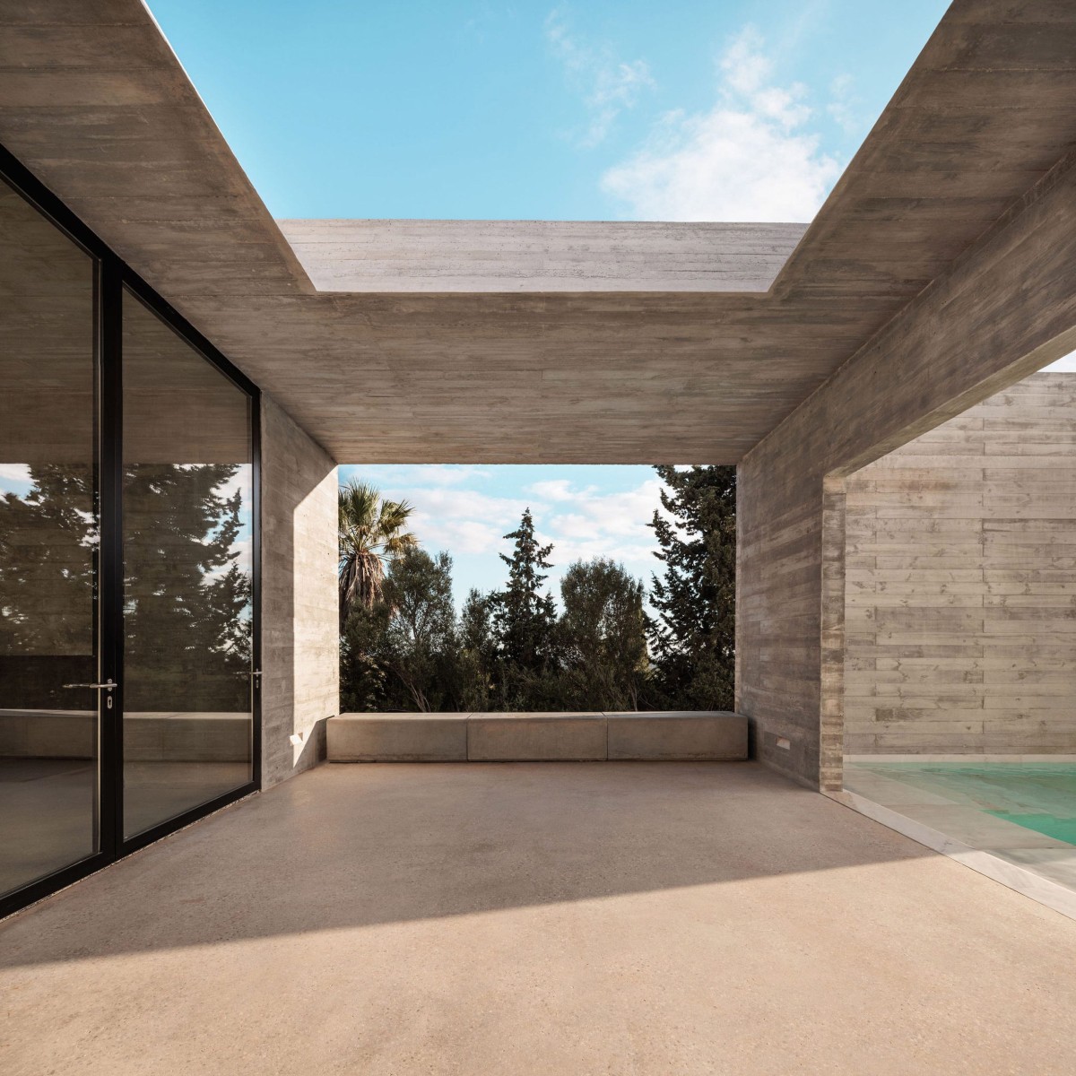 Mediante puertas giratorias de cristal se accede del salón a una terraza protegida por una pérgola de hormigón.