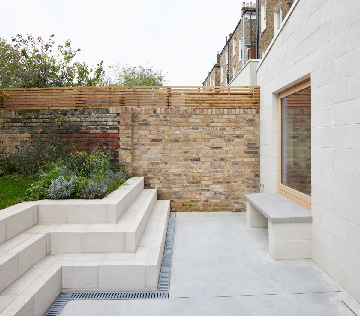 Junto a la pared exterior, hay un banco minimalista que hace juego con los bloques de mampostería de la ampliación.