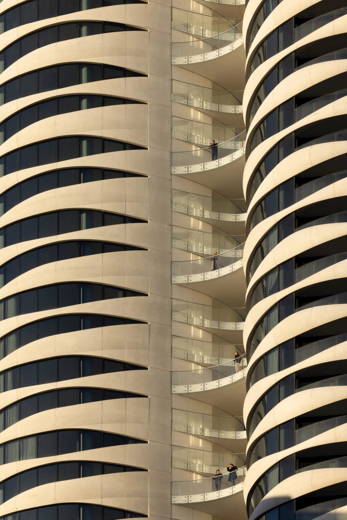 La torre está formada por cilindros rectos de vidrio y paneles de hormigón blanco, entre los cuales hay balcones y corredores abiertos.