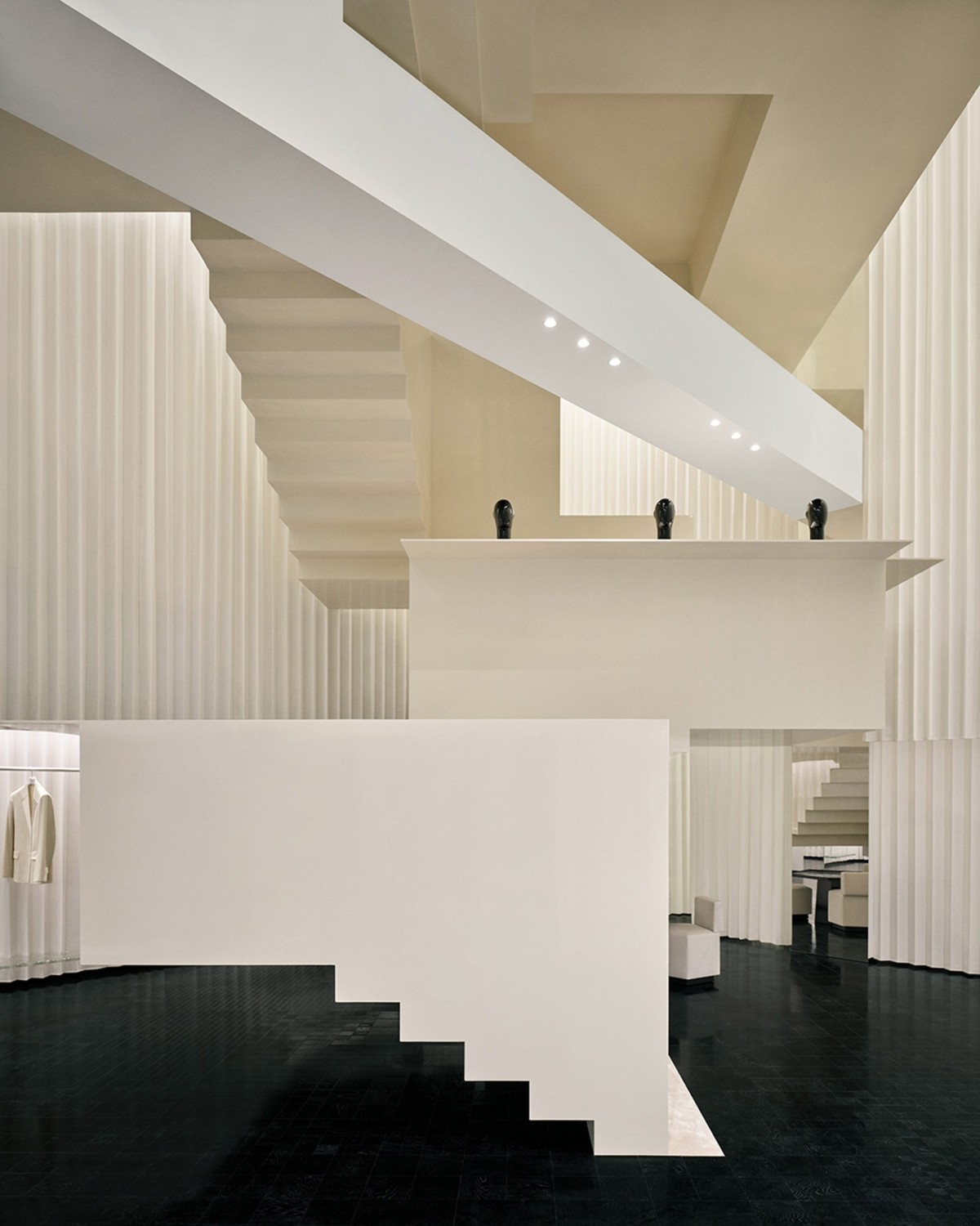 Las paredes plisadas continúan la relación con el exterior, acentuando la verticalidad y guiando la mirada hacia el corazón del espacio: una escalera en zigzag.