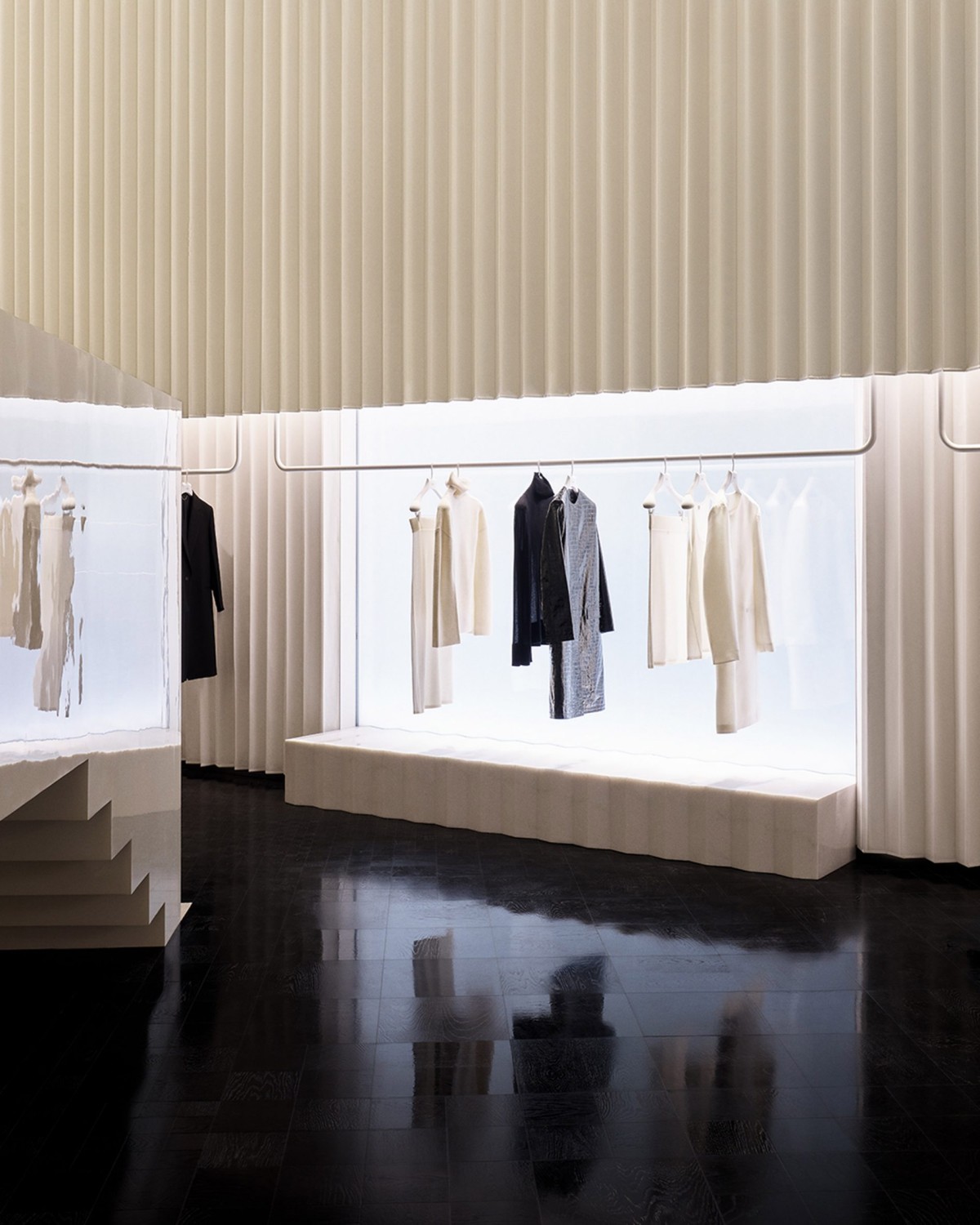 Los productos expuestos, como ropa, bolsos o joyas, se disponen con una estética casi museística sobre pedestales blancos y maniquíes translúcidos.