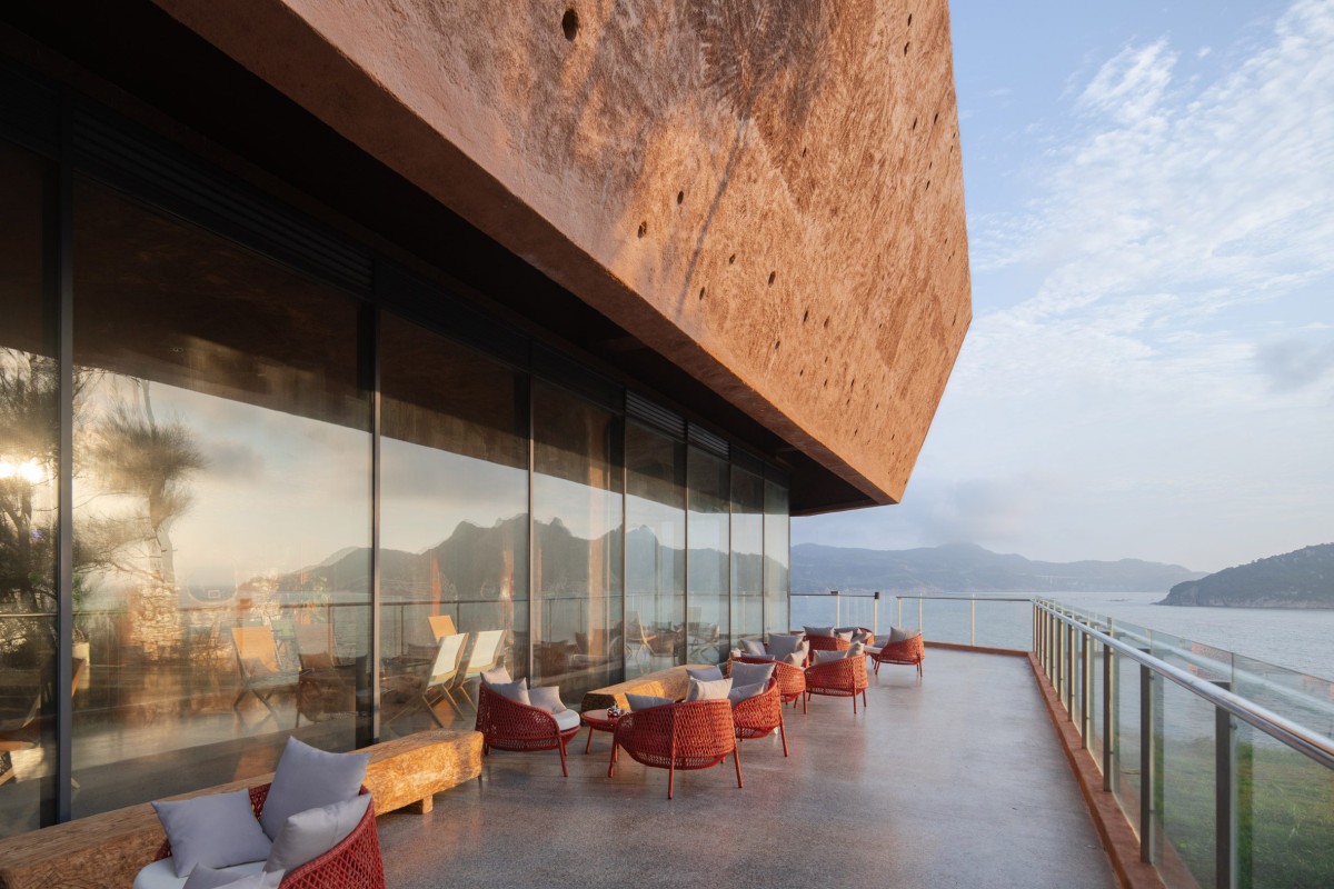 Una terraza exterior prolonga este espacio hacia el océano, protegida parcialmente por la cubierta y delimitada por una barandilla de cristal.