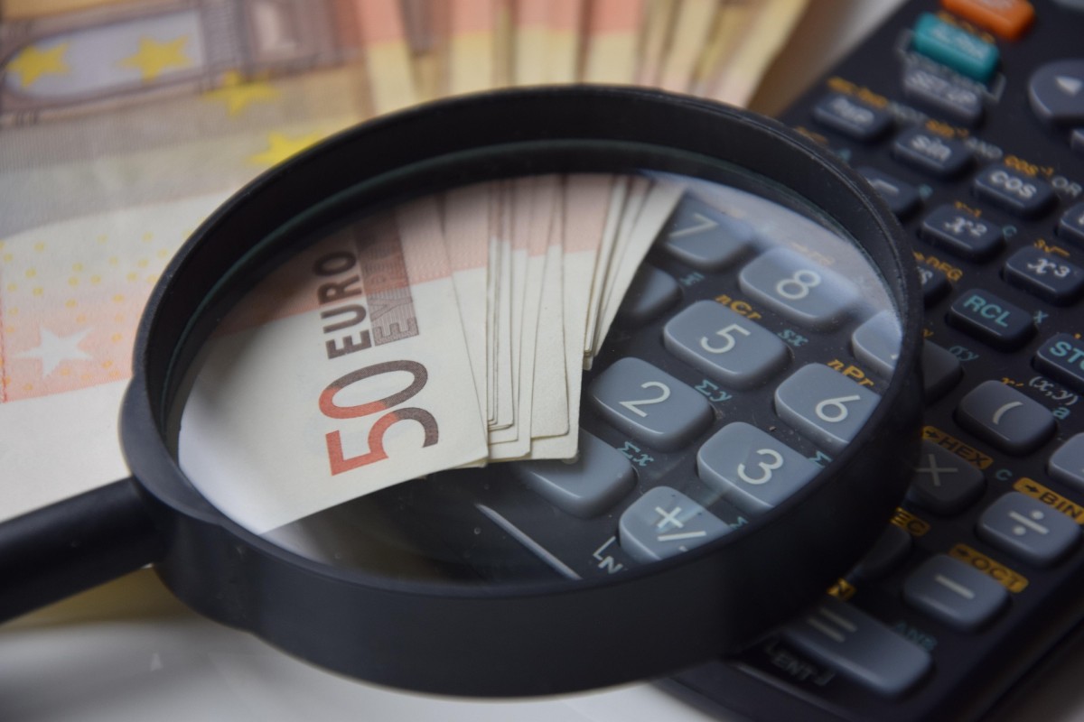 Cómo afecta no aceptar una herencia al Impuesto de Sucesiones Lupa y calculadora junto a billetes de 50 euros sobre una mesa