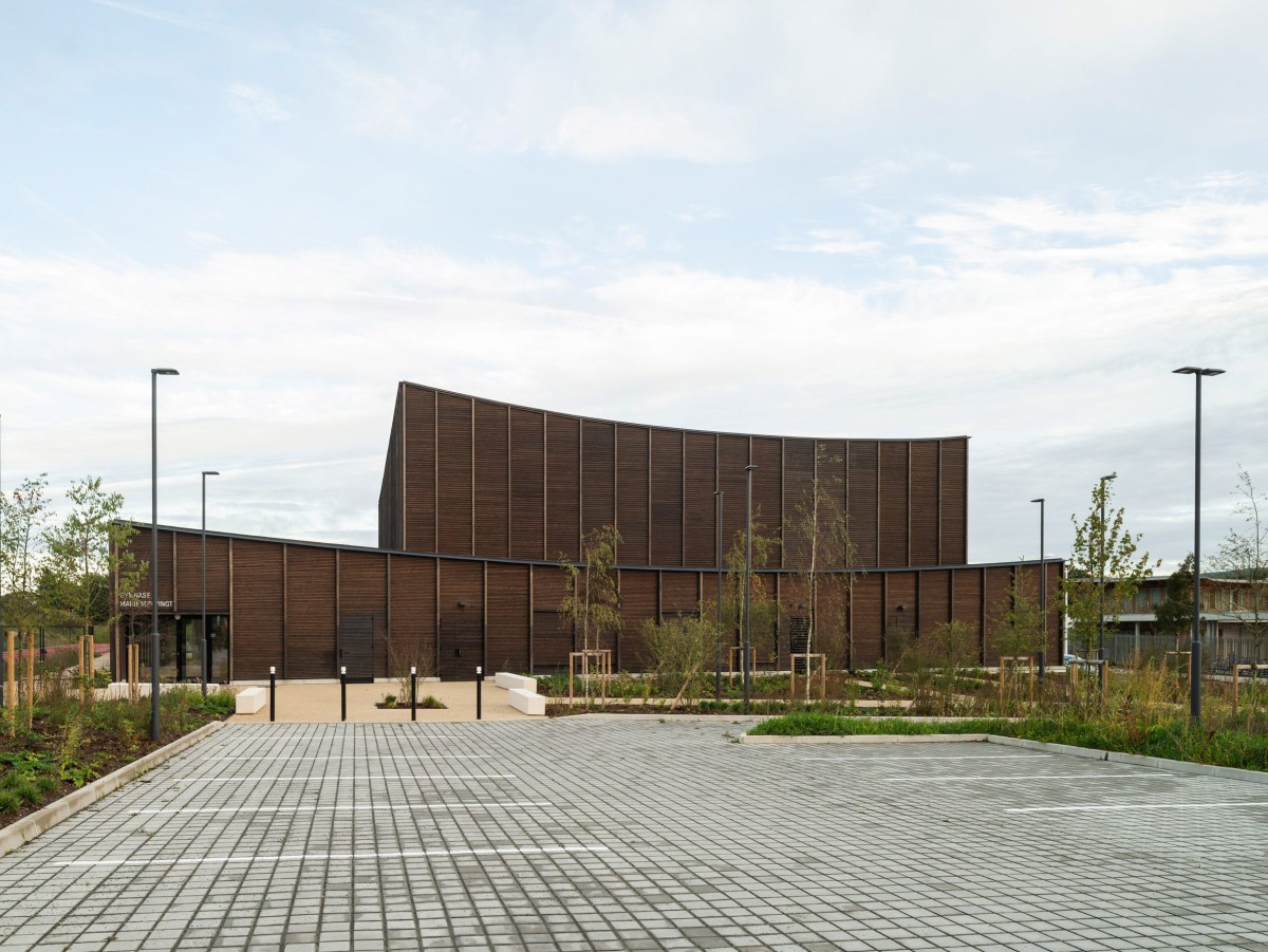 El complejo incluye, además del edificio deportivo, pistas de atletismo exteriores y una zona de aparcamiento ajardinada que conecta con el entorno rural.