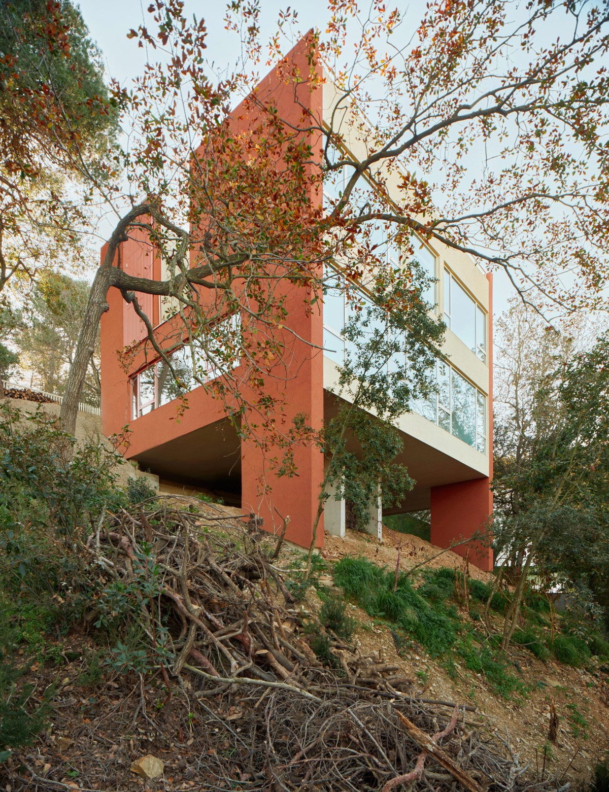 La vivienda consta de dos plantas apoyadas en esbeltas columnas de hormigón que elevan la estructura sobre la ladera.