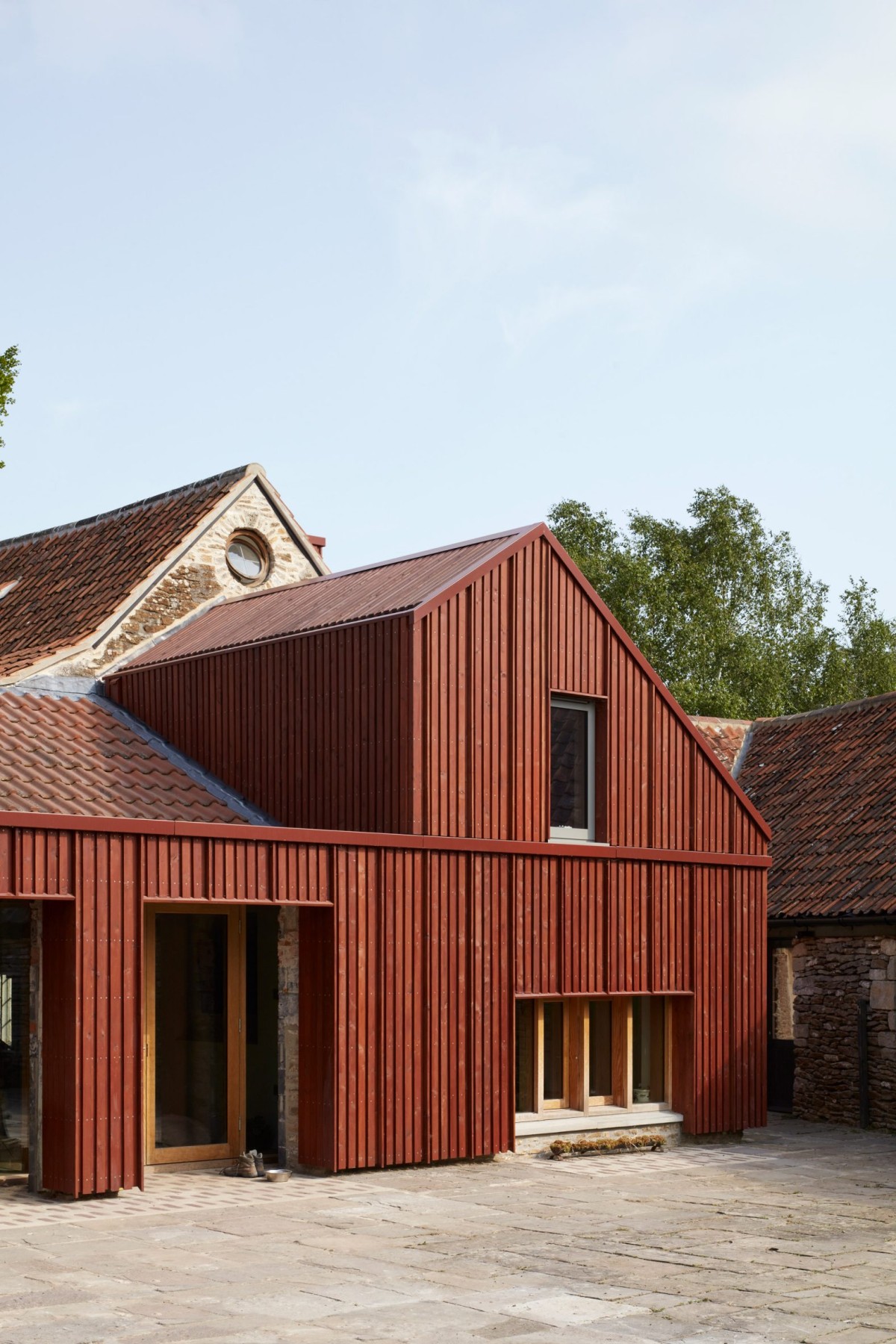El techo de terracota de los años 80 se integró con un revestimiento de madera teñida de rojo, creando una conexión respetuosa pero audaz.