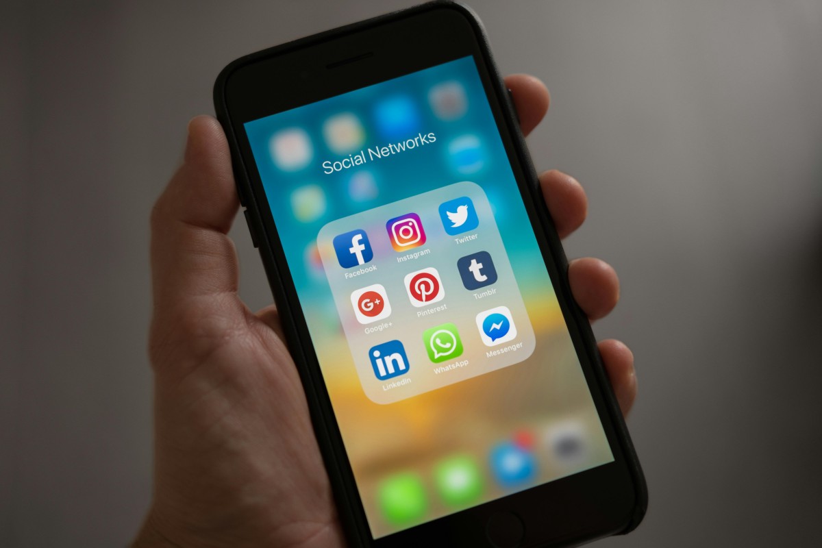 Deducción de gastos en redes sociales para autónomos en el IRPF Mano de una autónomo sosteniendo un móvil con aplicaciones de redes sociales