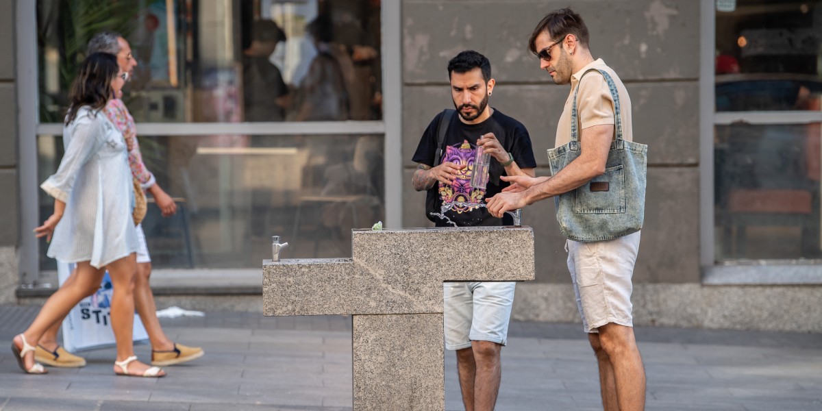 Dos hombres rellenado una botella en una fuente pública