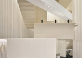 Las paredes plisadas continúan la relación con el exterior, acentuando la verticalidad y guiando la mirada hacia el corazón del espacio: una escalera en zigzag.