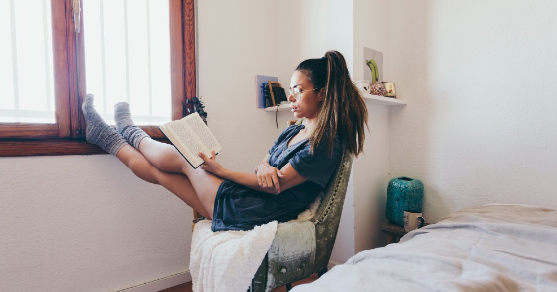 Chica leyendo en habitación alquilada - Archivo