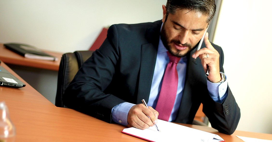 Contador-partidor firmando documentos de una herencia mientras atiende una llamada