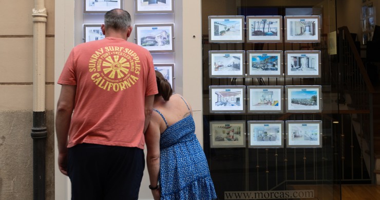 Archivo - Dos personas observan los anuncios de viviendas en venta en una inmobiliaria. 