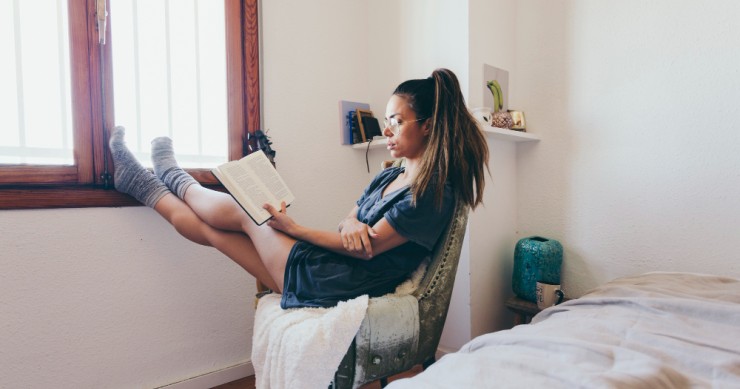 Chica leyendo en habitación alquilada - Archivo