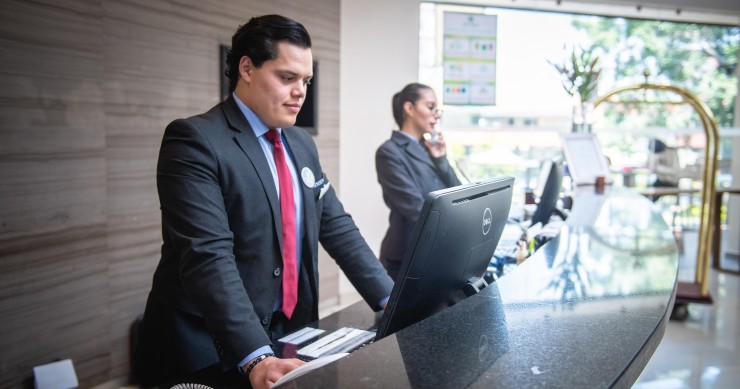 La verificación de identidad de los huéspedes debe ser acorde a la normativa Dos recepcionistas de hotel verificando la identidad de un huésped en el mostrador
