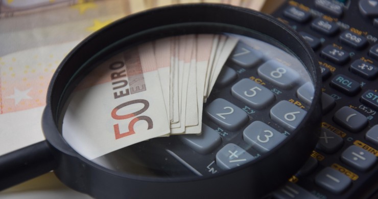 Cómo afecta no aceptar una herencia al Impuesto de Sucesiones Lupa y calculadora junto a billetes de 50 euros sobre una mesa