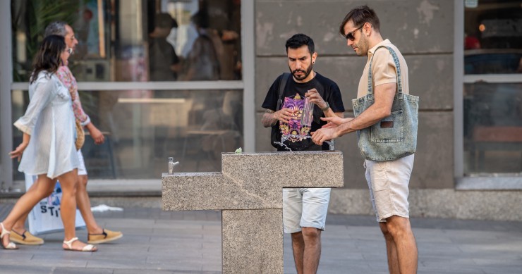 Dos hombres rellenado una botella en una fuente pública