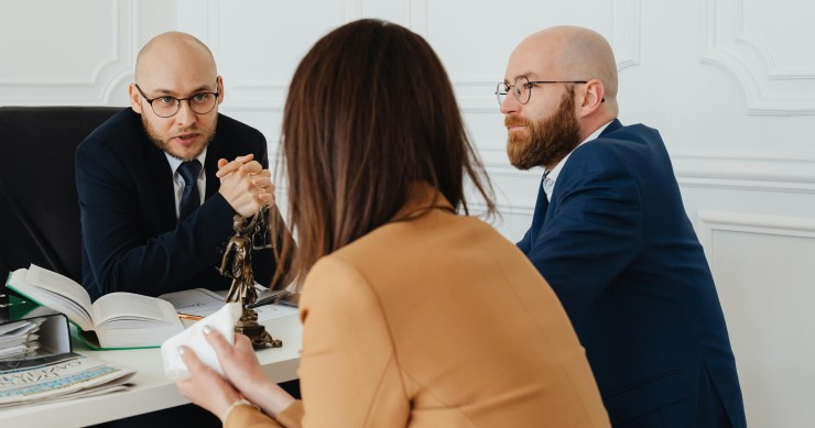 Dos hombres y una mujer reunidos en una mesa revisando documentos durante una negociación hipotecaria