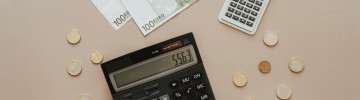 Dues calculadores amb bitllets i monedes d'euro representant el càlcul de l'IBI d'un habitatge